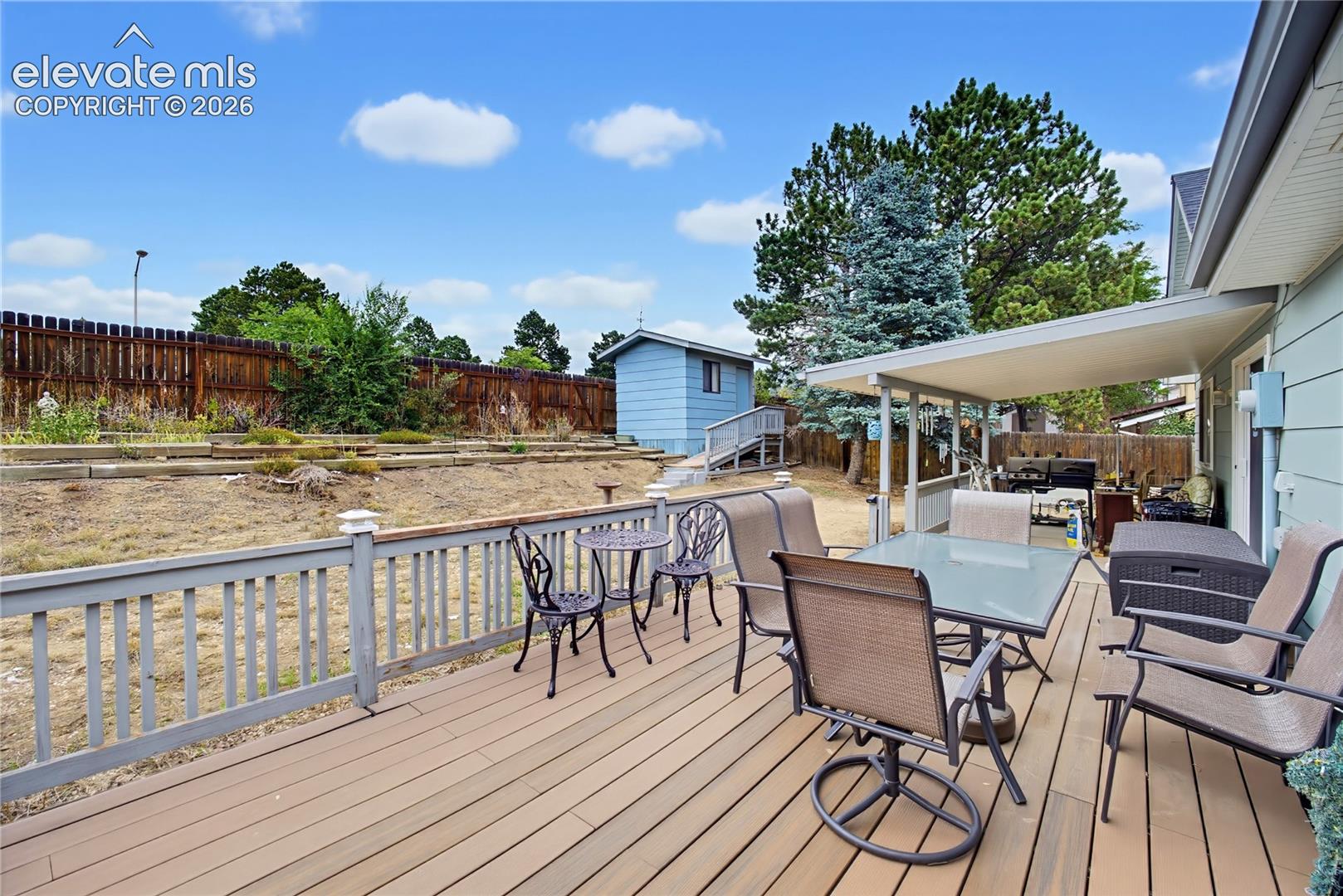 Expansive wood-finish deck with a solid railing, covered patio area, and a detached shed