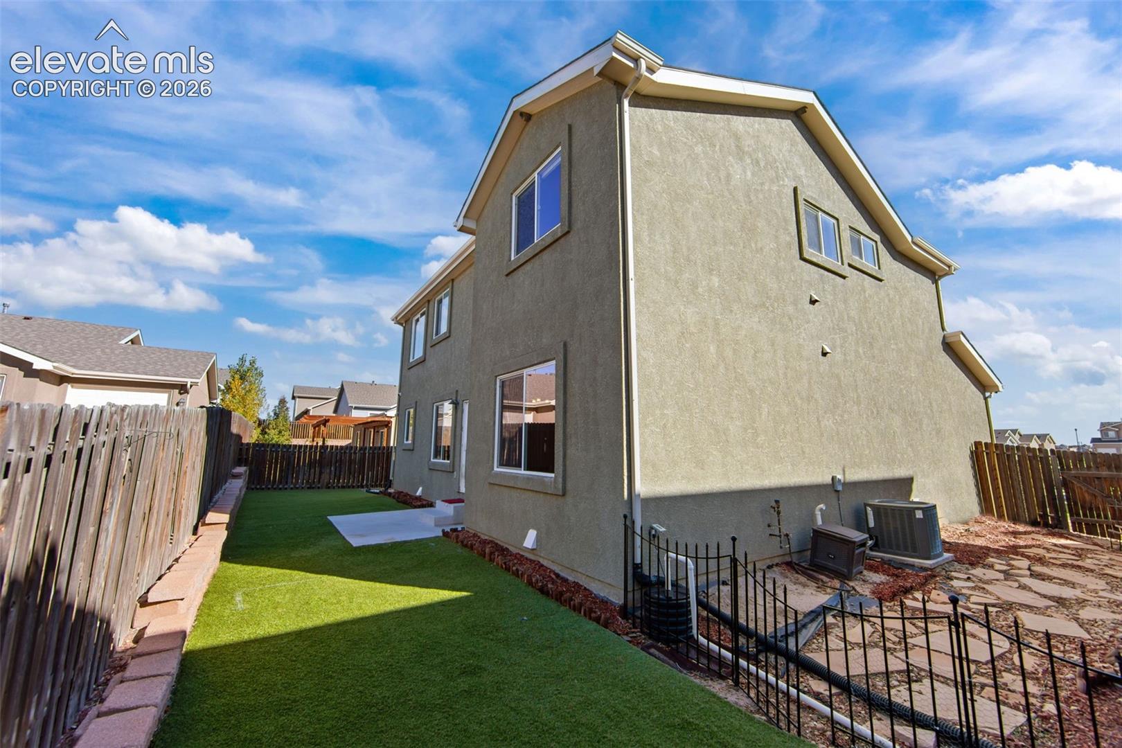 Stucco exterior siding, low-maintenance artificial turf, flagstone hardscaping, concrete patio, and metal perimeter fencing