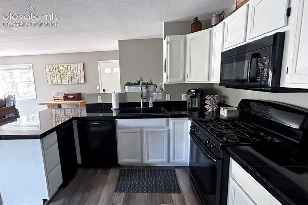 Kitchen featuring LVP flooring, white cabinetry, black granite tile countertops, and black appliances