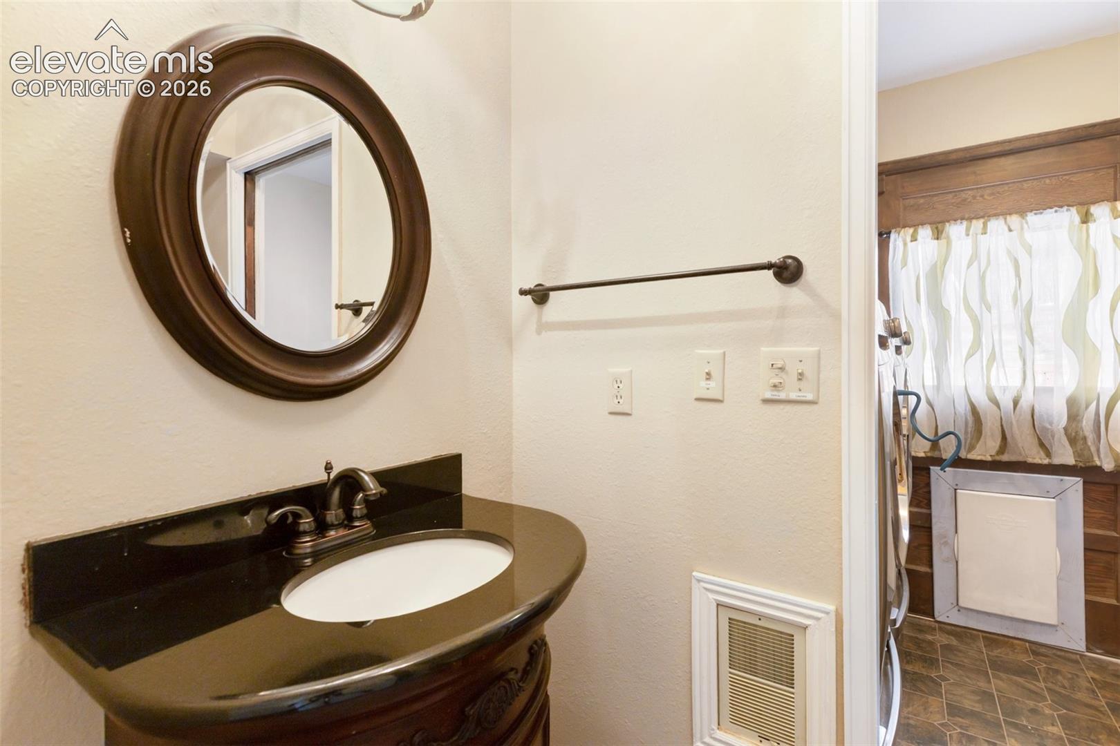 Vanity with a dark countertop, an oval undermount sink, and a bronze-finish faucet