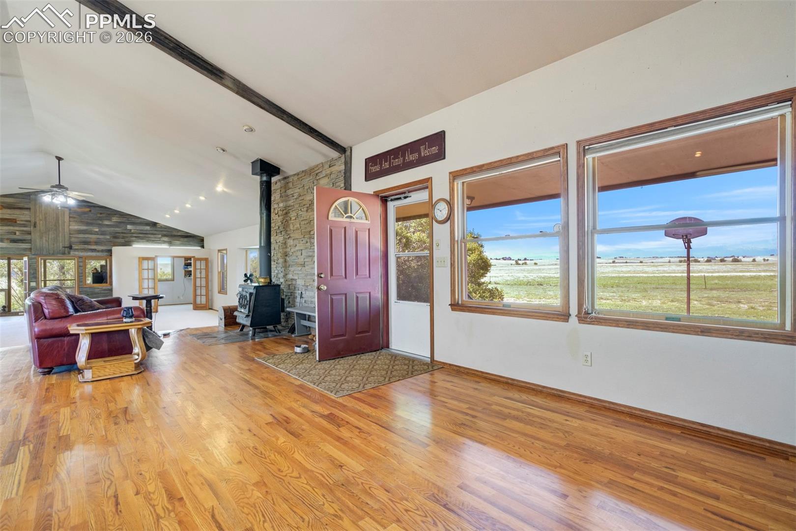 Hardwood flooring throughout a spacious room featuring a vaulted ceiling with exposed beams