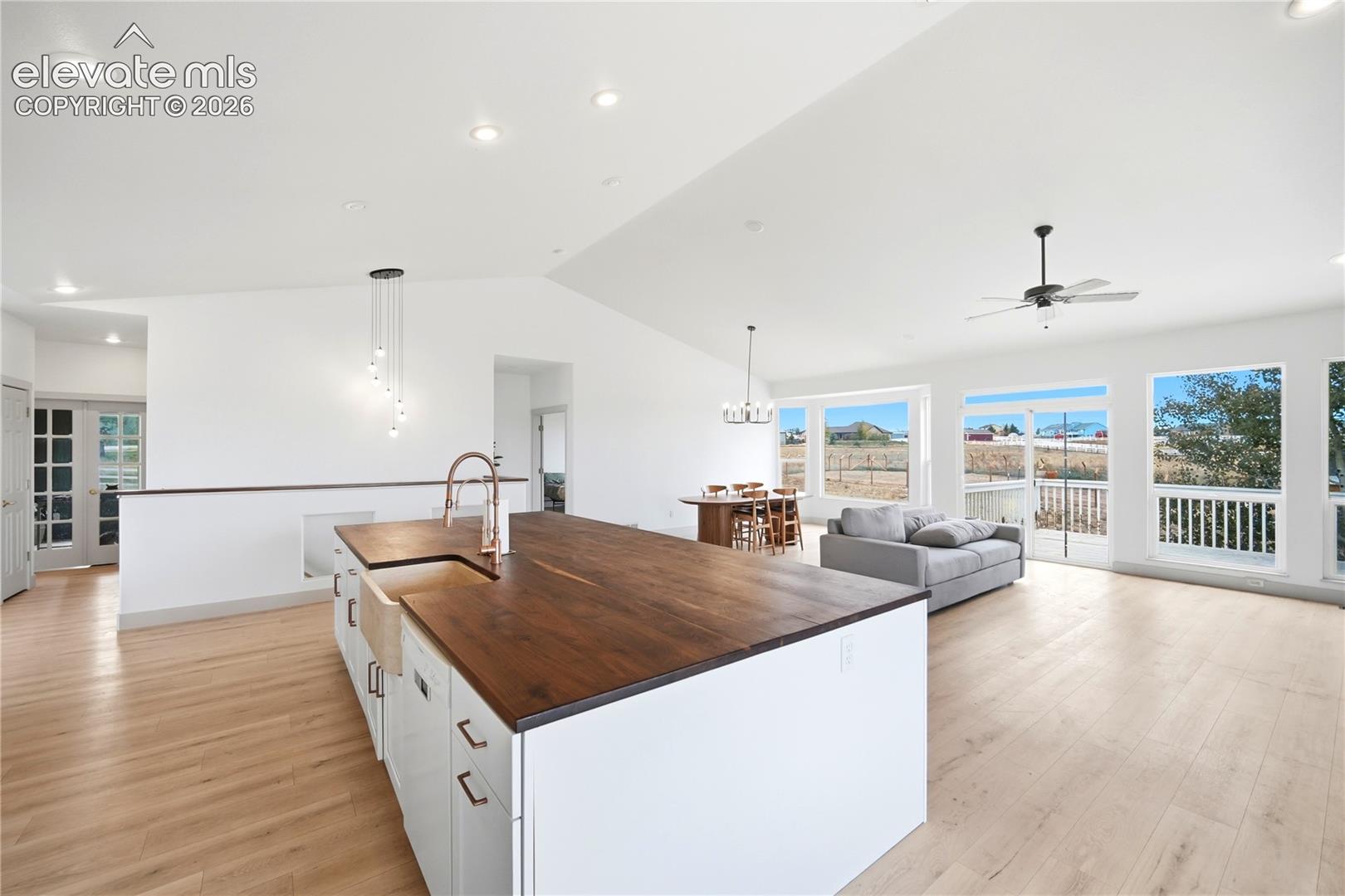 Open-concept kitchen featuring an oversized island with a dark wood countertop, apron-front sink, recessed lighting, vaulted ceilings, and wood-finish flooring