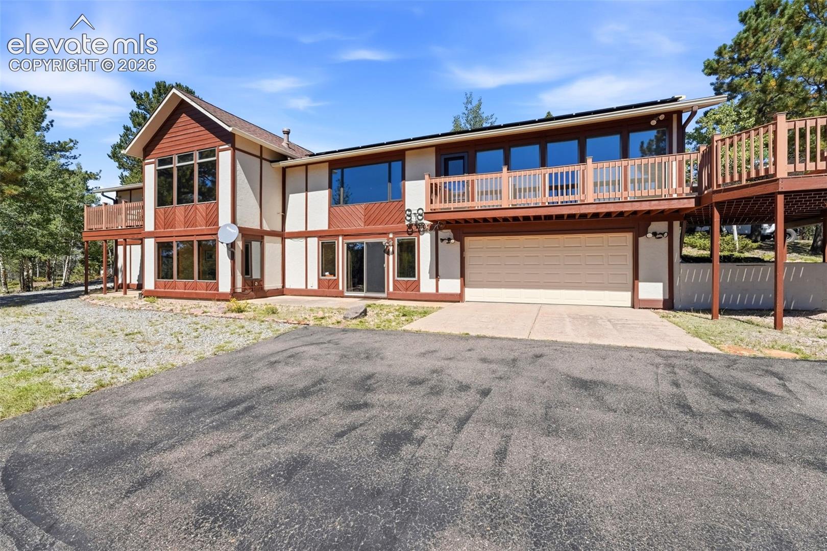 Multi-level residential exterior with wood paneling and stucco siding, featuring multiple decks with wood railings, an attached garage, and an asphalt driveway
