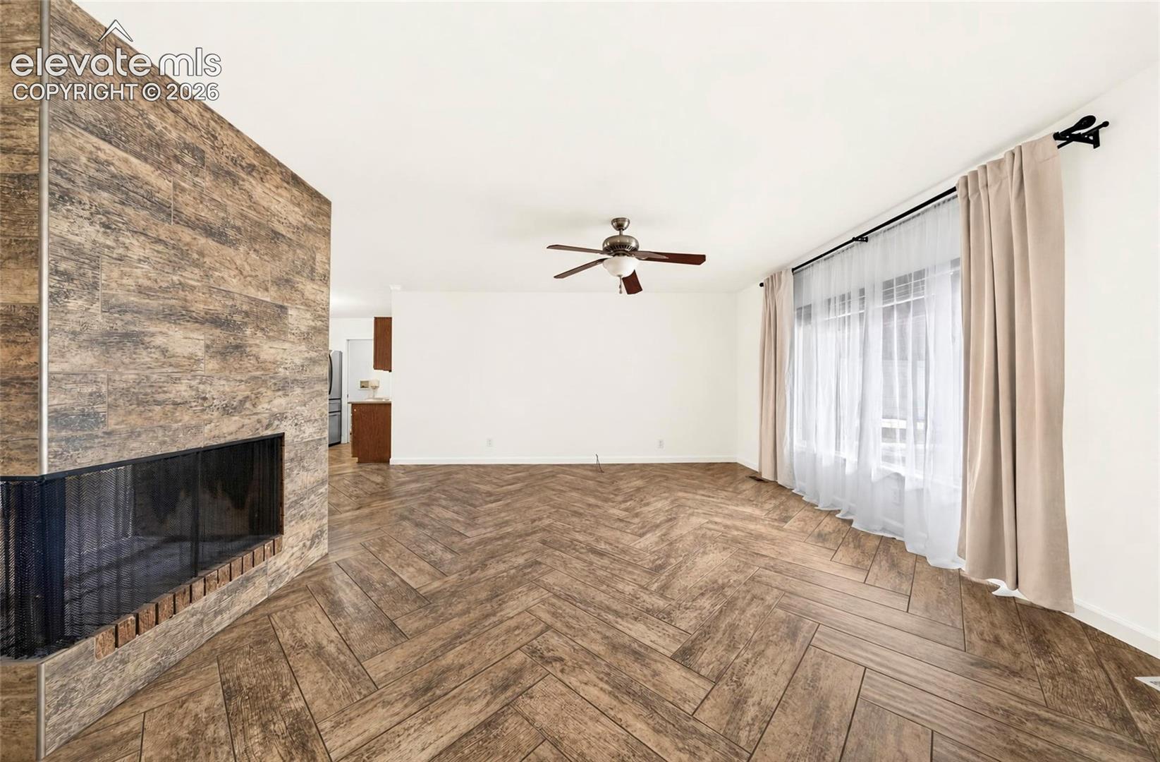 Herringbone-pattern wood-finish flooring, floor-to-ceiling wood-finish fireplace surround, and a ceiling-mounted light fixture with integrated fan