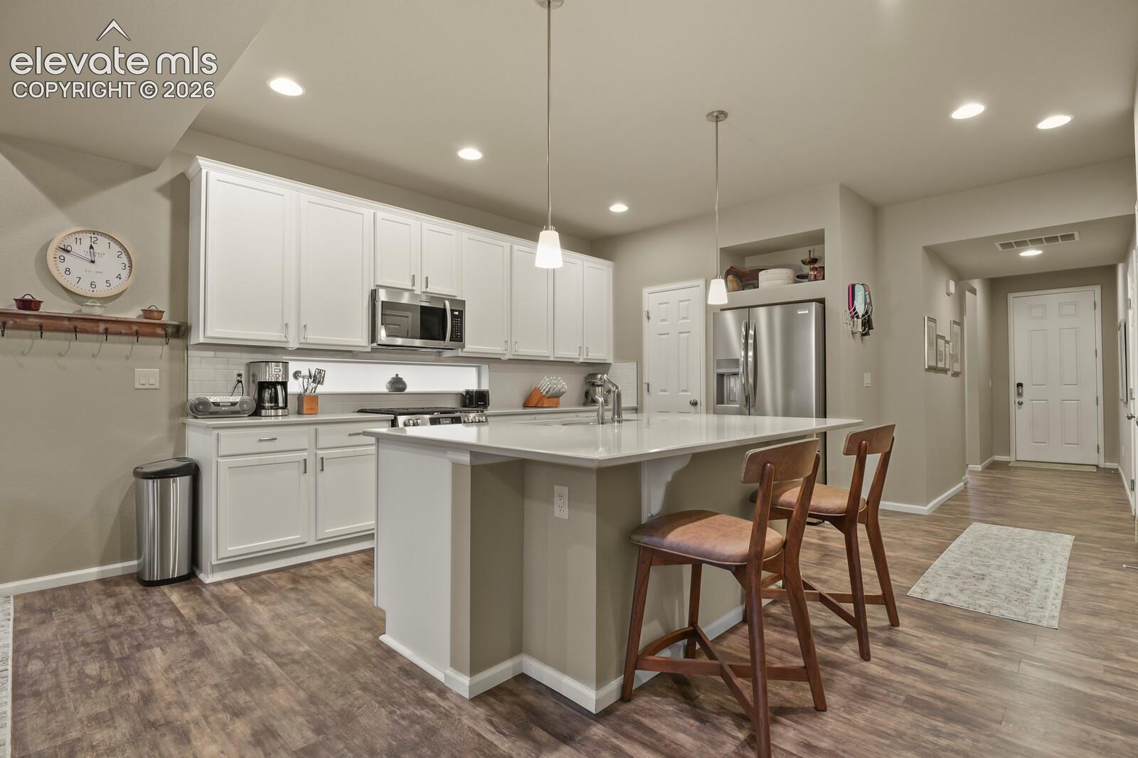 Kitchen featuring white cabinetry, an expansive center island with Quartz countertop, Upgraded stainless steel appliances, recessed lighting, and wood-finish luxury tile flooring