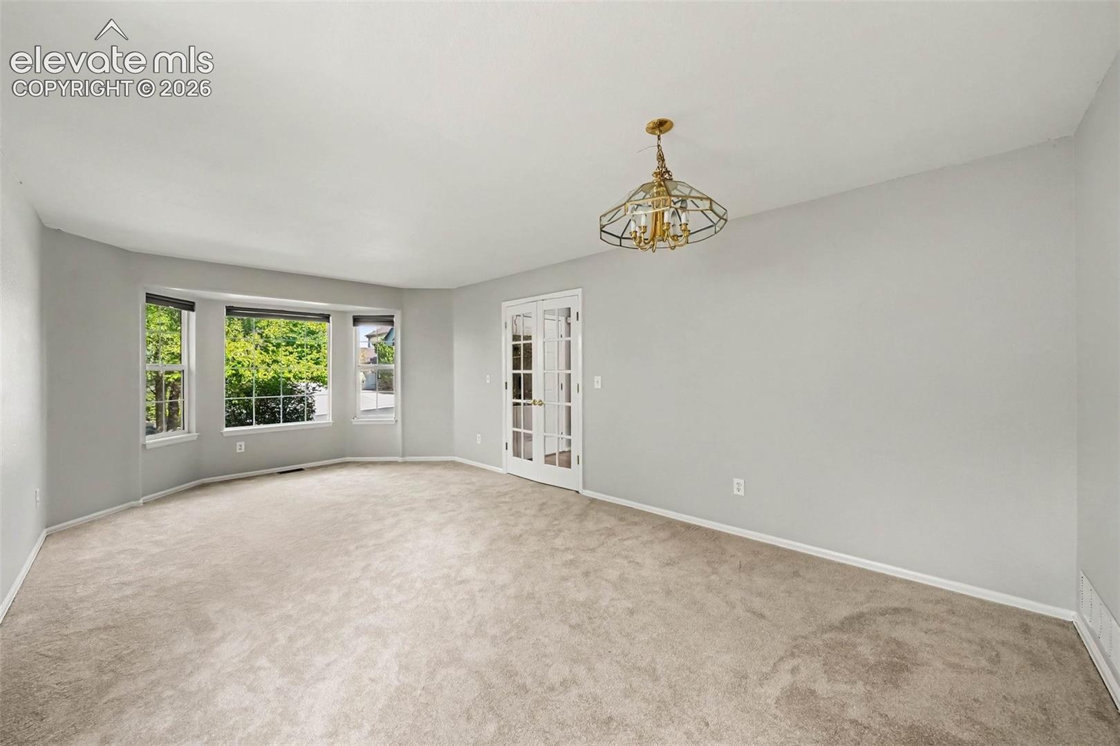 Carpeted room with a bay window, a brass-toned chandelier, and French doors
