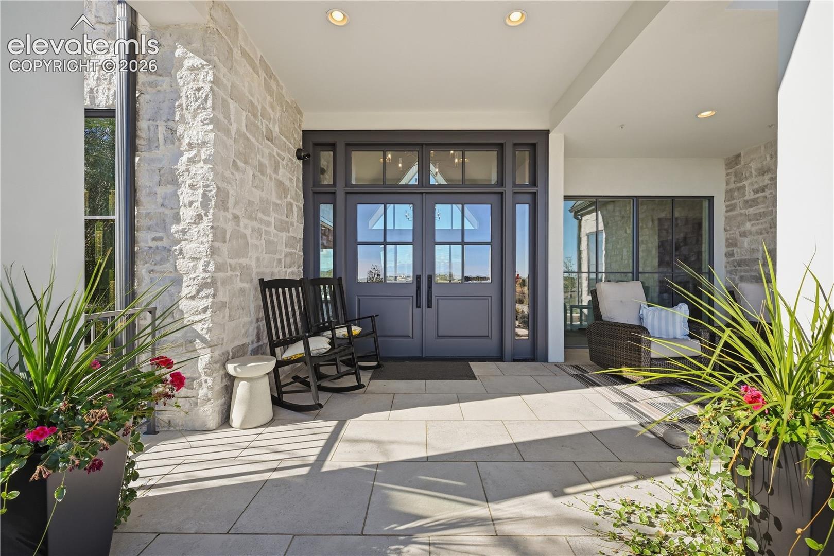 Covered entryway featuring natural stone wall cladding, large-format stone paver flooring, recessed lighting, and a double-door entry with glass transom and sidelights