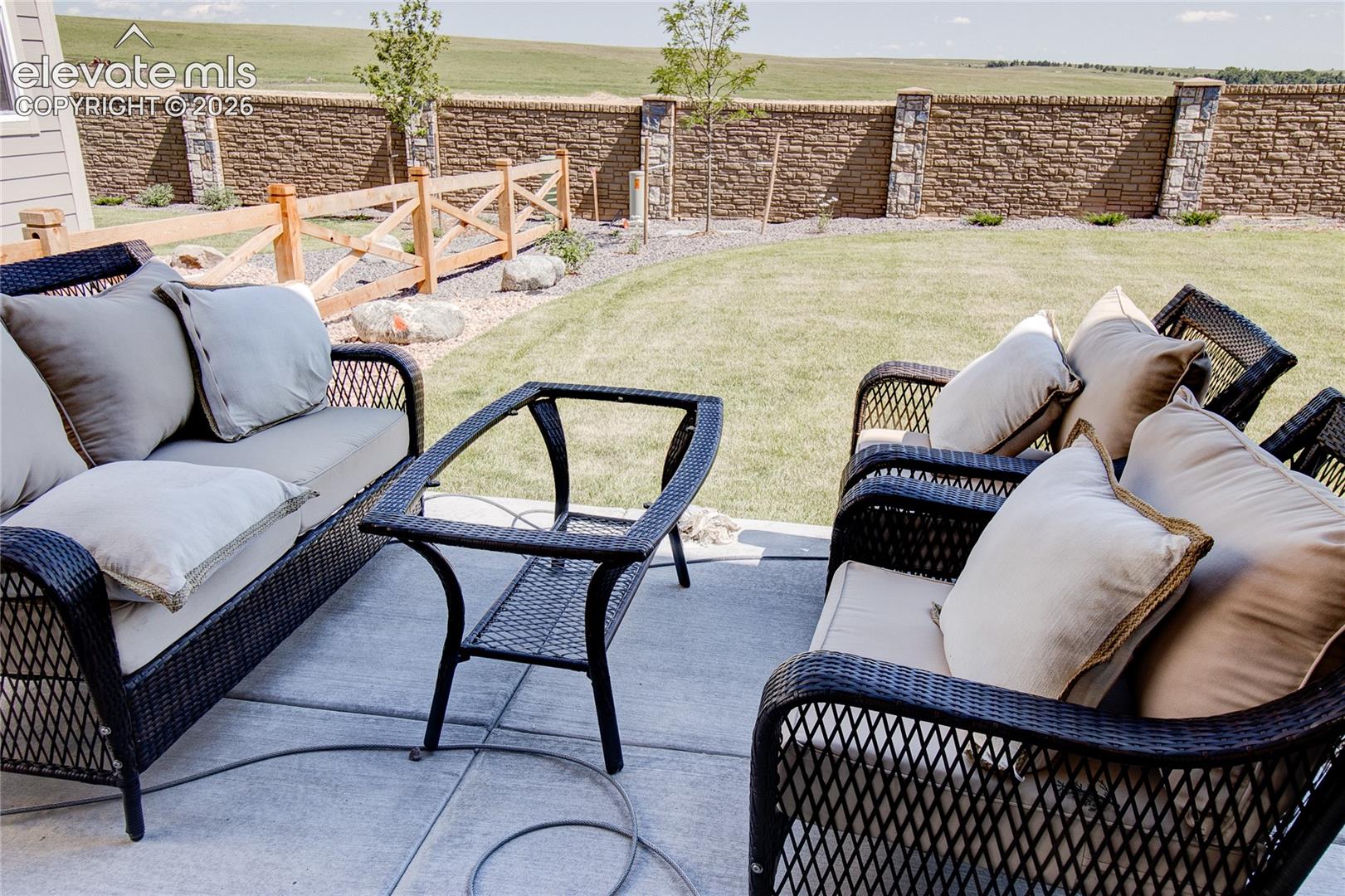 Concrete patio featuring a manicured lawn, stone perimeter wall with stone-accented pillars, and wood-rail fencing