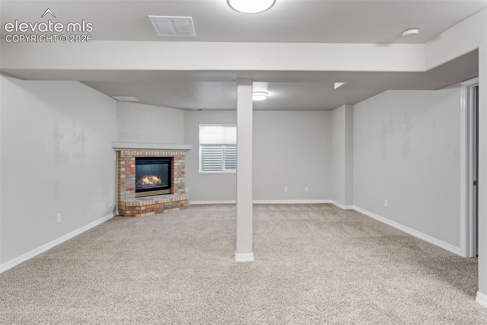 Open-concept area featuring neutral carpeting, a brick-surround corner fireplace with a masonry hearth, and a structural support column