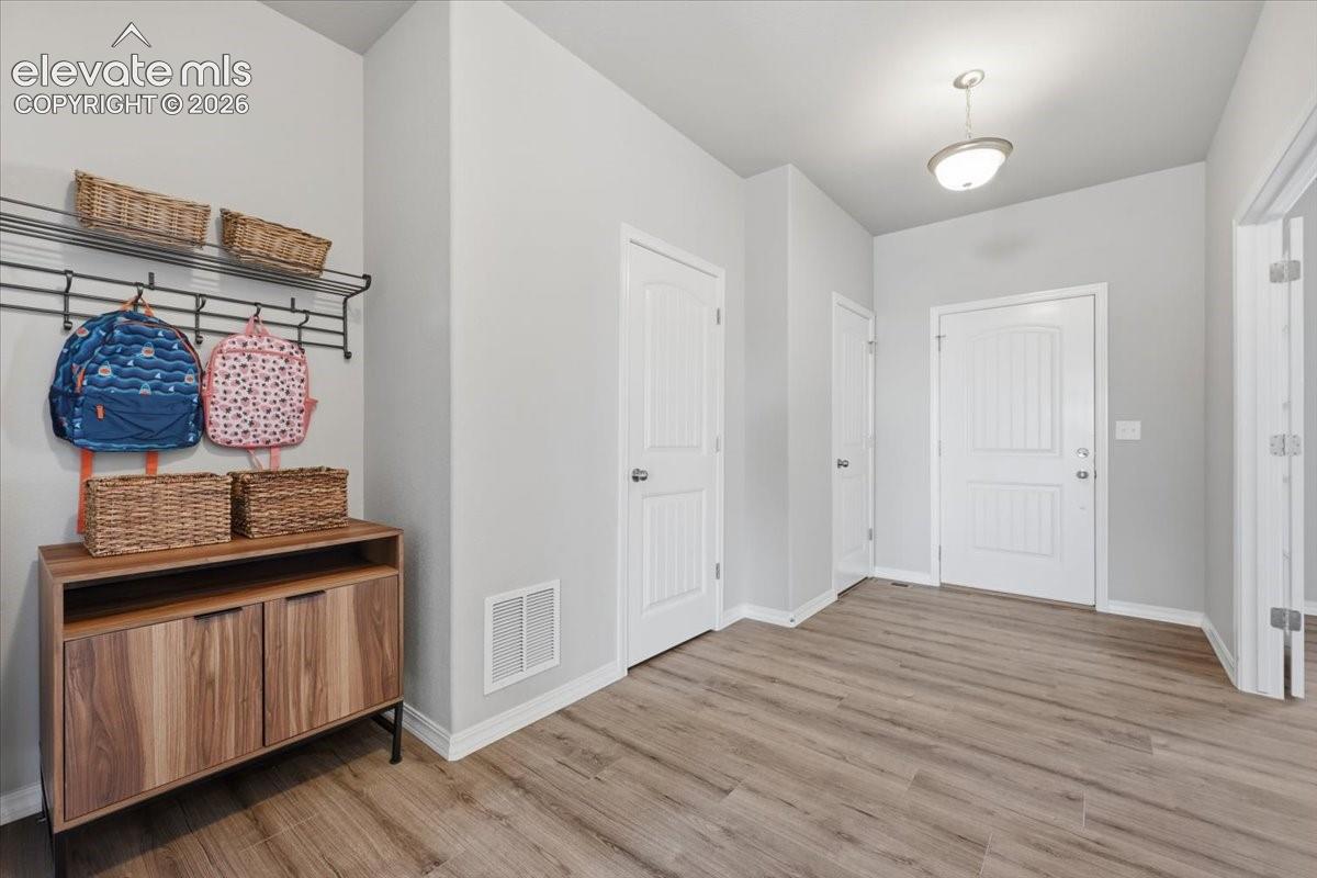 Entryway featuring wood-finish flooring, a neutral color palette, paneled interior doors, and a wall-mounted metal organizational rack with an integrated upper shelf