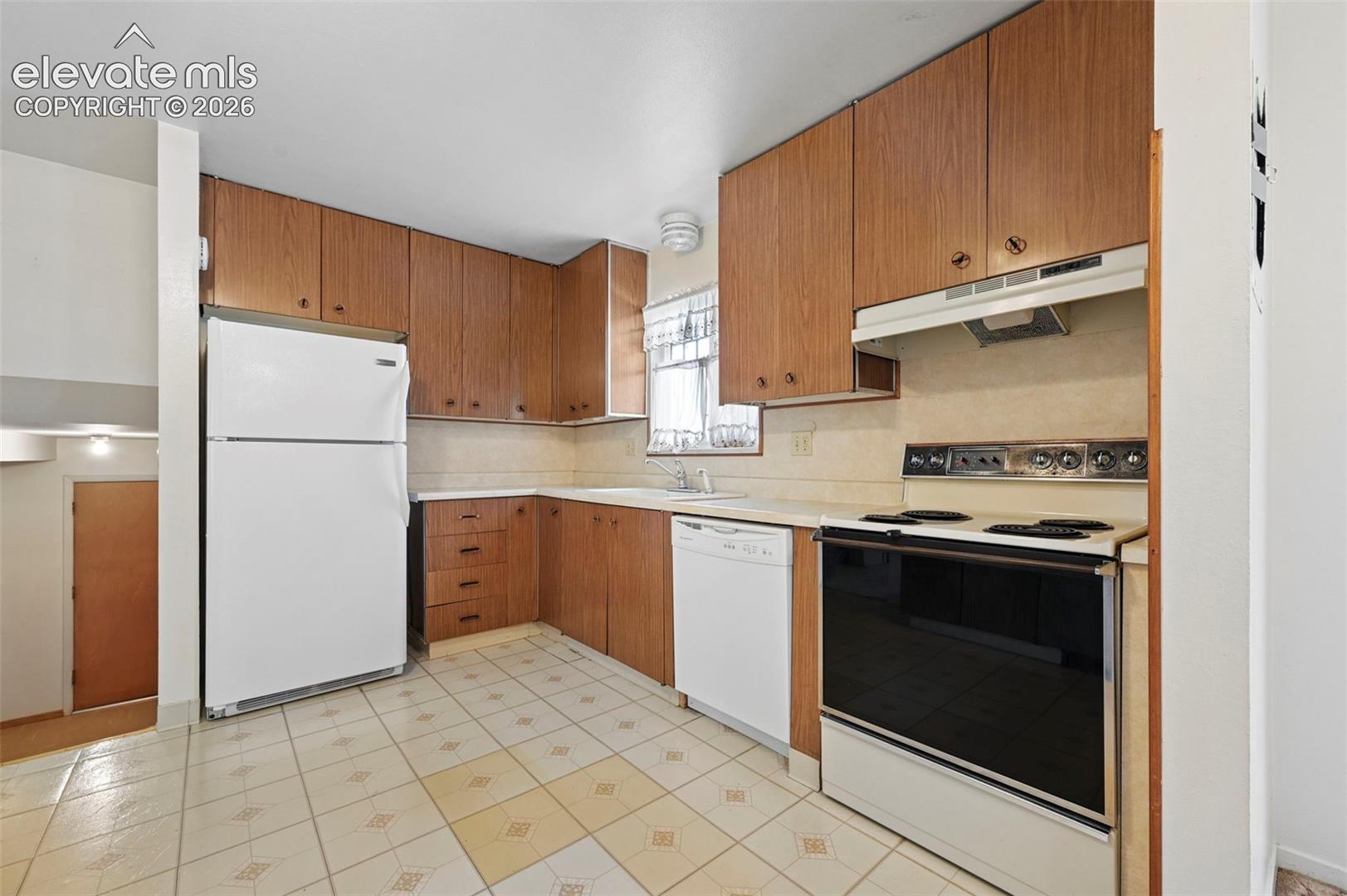 Kitchen featuring wood cabinetry, white appliances, integrated range hood, solid surface countertops, and vinyl flooring