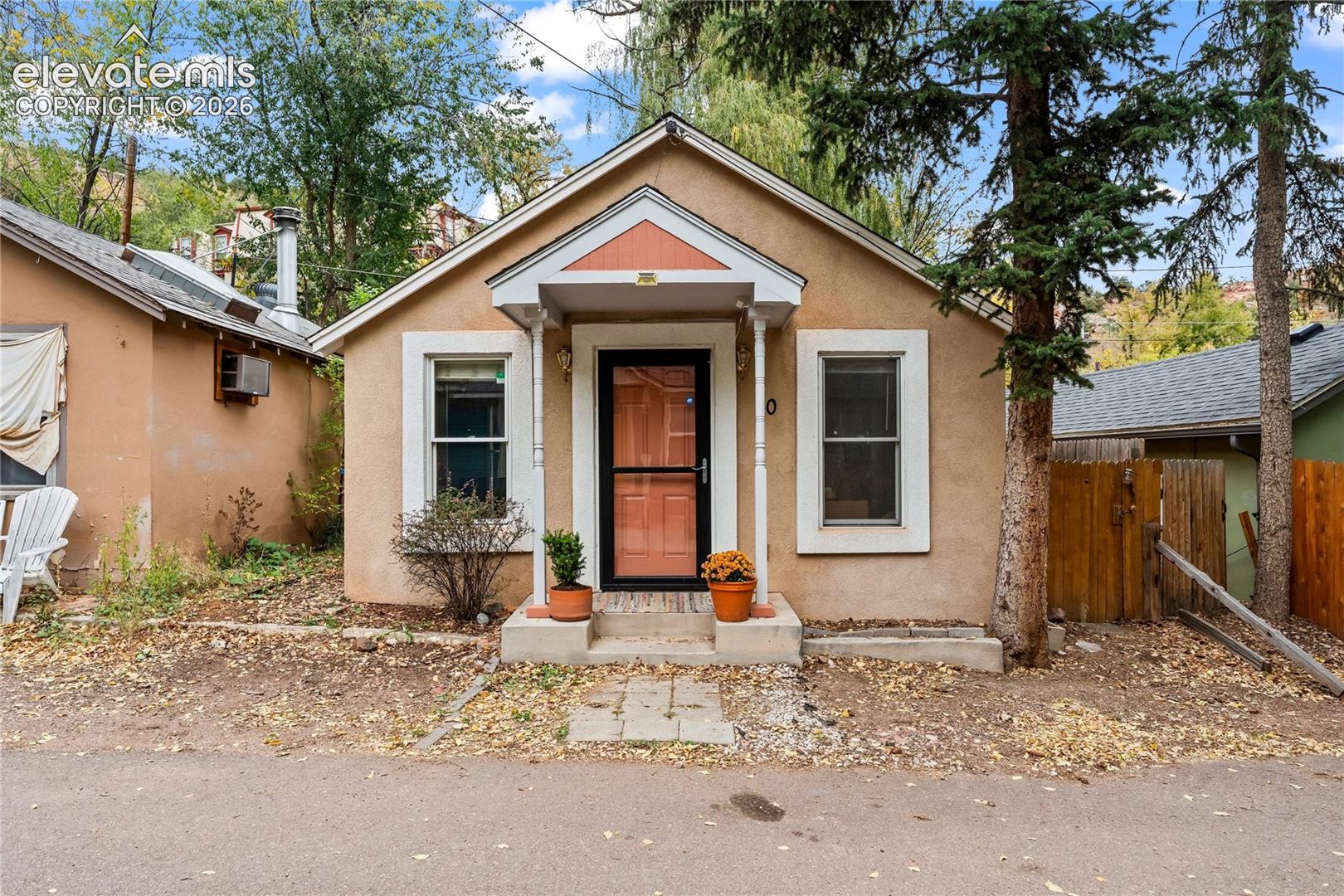Stucco exterior featuring a gabled roofline, a covered front entryway with decorative support pillars, and white window trim