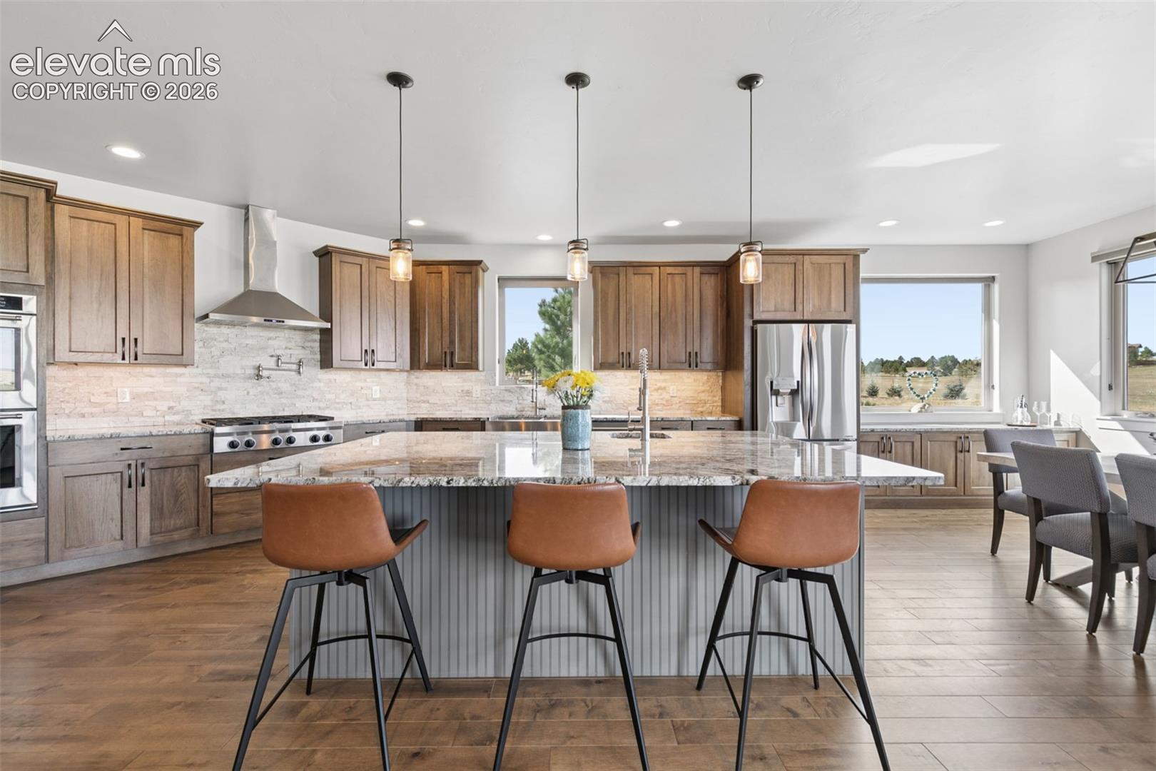 Gourmet kitchen featuring a large central island with seating, stainless steel appliances, wood-finish flooring, and ample cabinetry