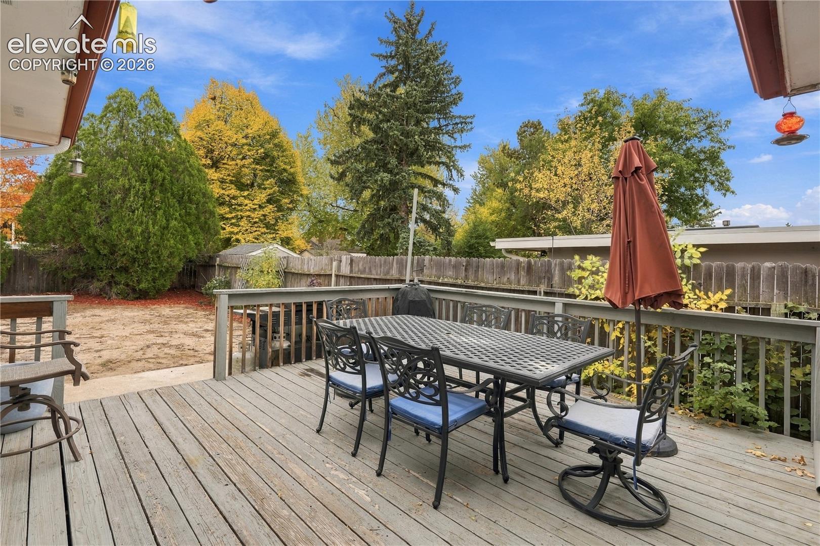 Elevated wood deck featuring a perimeter railing, partial roof overhang, and wood fencing