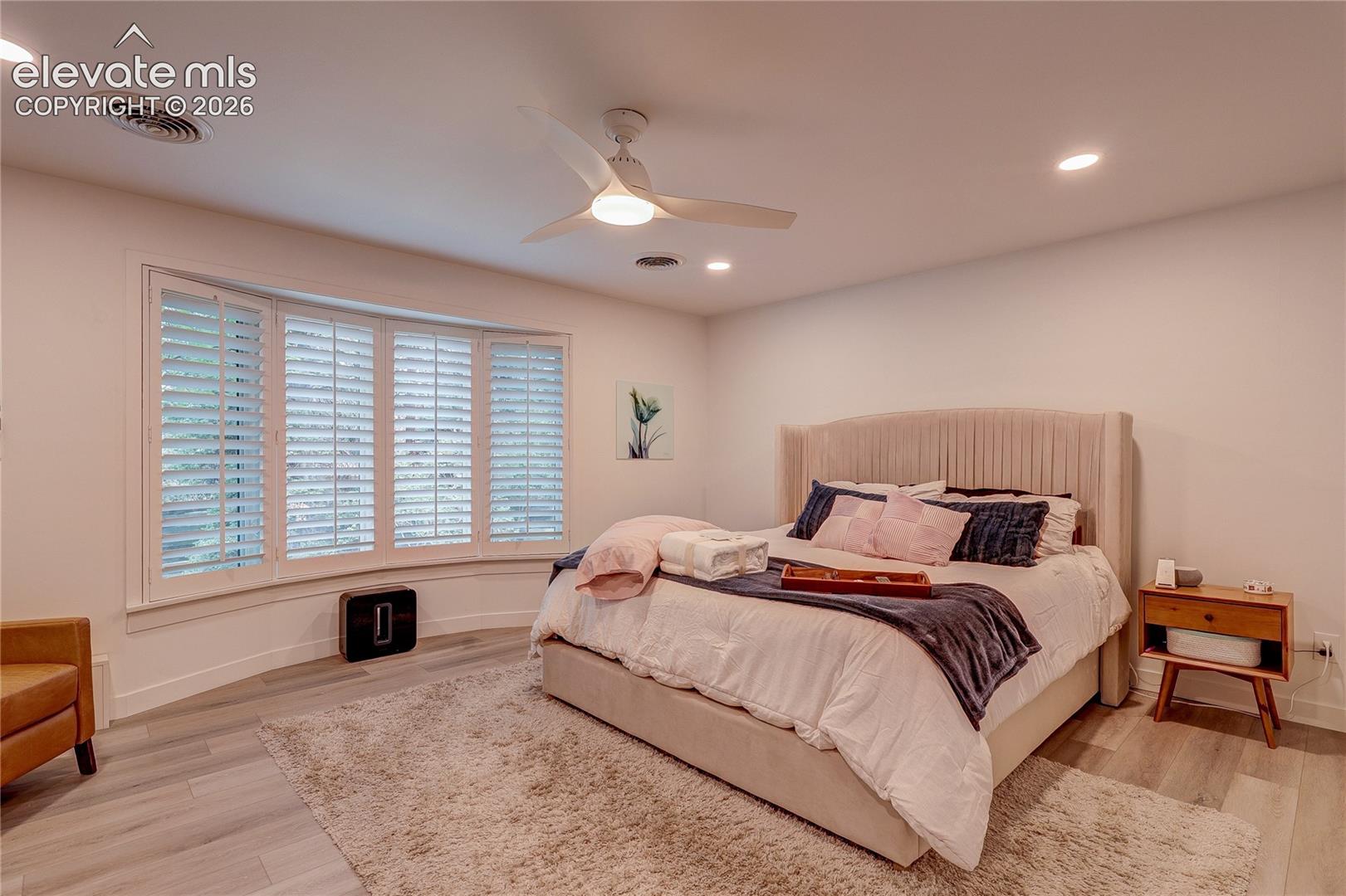 Bay window with white plantation shutters, wood-finish flooring, ceiling fan, and recessed lighting