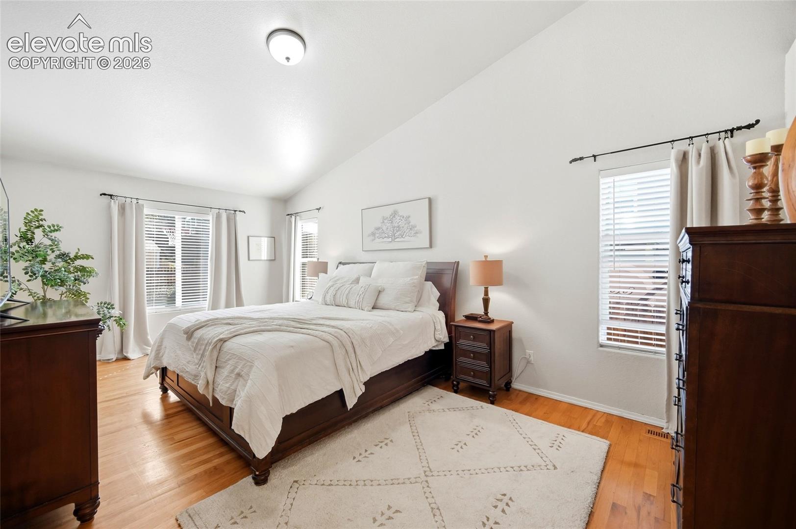 Vaulted ceiling, wood-finish flooring, and multiple windows with blinds