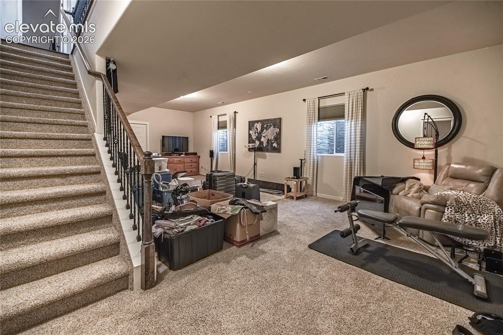 Open-concept interior space featuring neutral wall-to-wall carpeting and an open staircase with a metal balustrade and wood-finish handrail