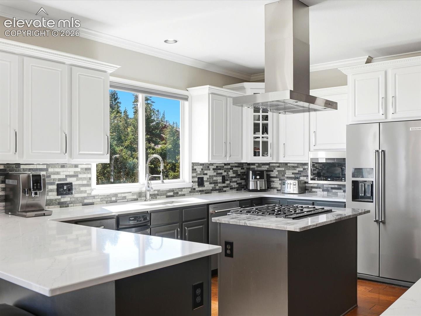 Kitchen featuring white upper cabinetry, multi-tone glass tile backsplash, stone countertops, central island with a built-in cooktop, and stainless steel hood range
