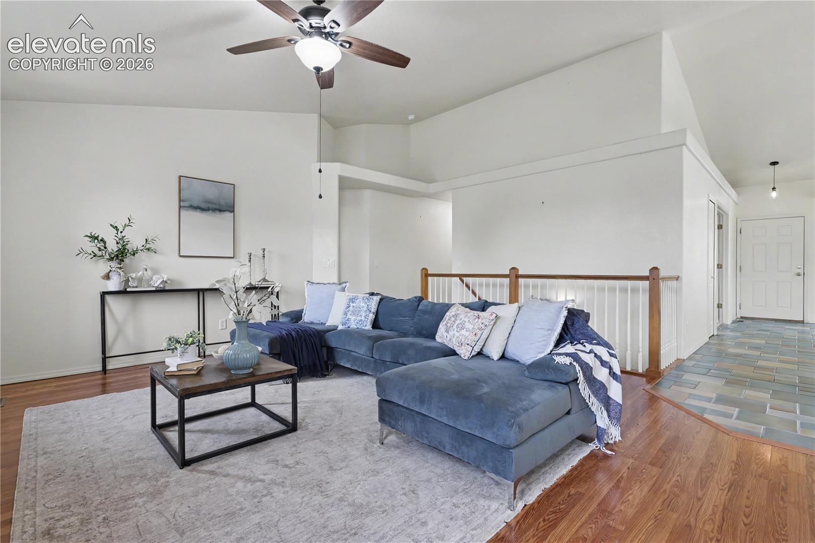 Vaulted ceiling living space featuring wood-finish flooring and a ceiling fan with integrated lighting