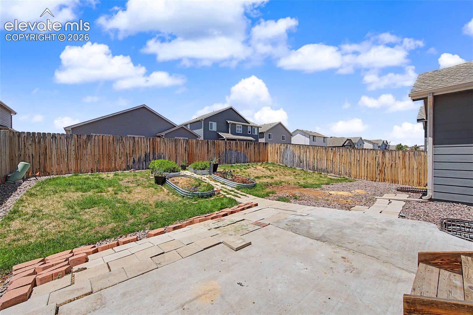 Expansive backyard featuring a concrete patio, brick edging, a wood privacy fence, and multiple raised garden beds