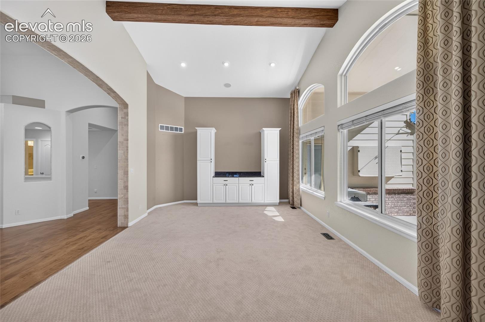 Vaulted ceilings featuring a structural wood beam, built-in white cabinetry with a dark surface, arched windows, and a tiled archway