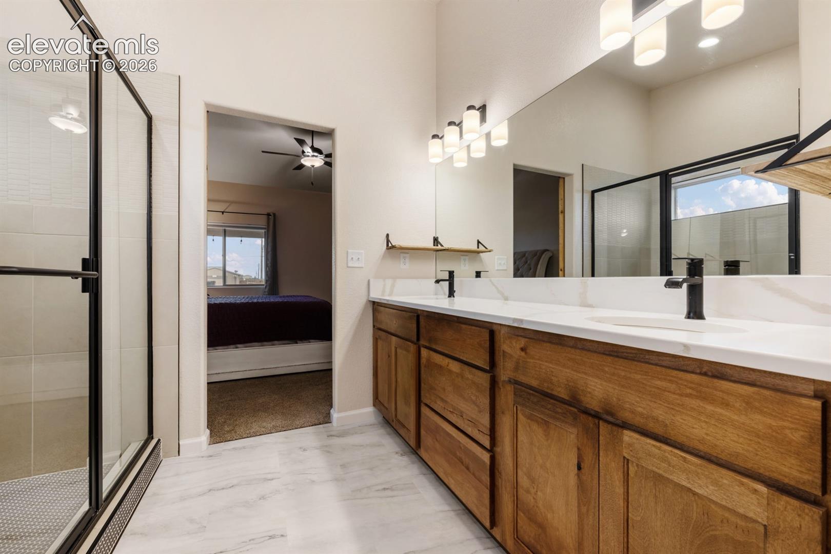 Double vanity featuring wood-finish cabinetry, solid-surface countertops, dual rectangular under-mount sinks, matte black plumbing fixtures, and a full-width mirror
