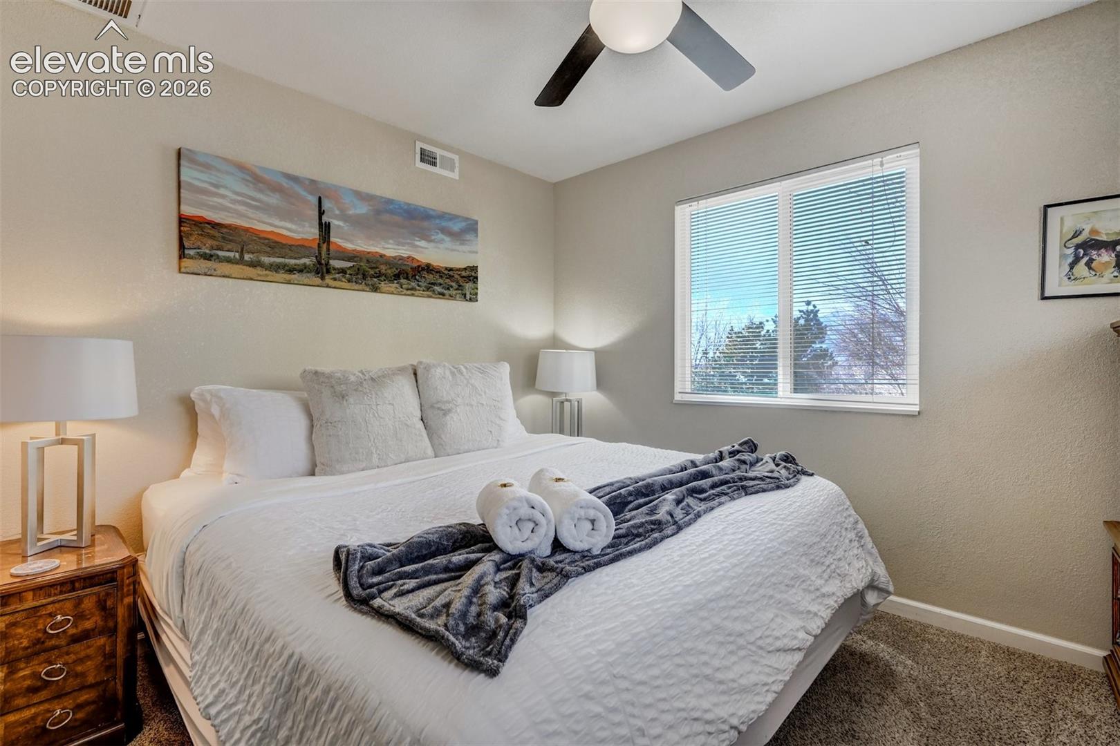 Neutral wall tones complement the window with blinds, ceiling fan, and carpeted flooring