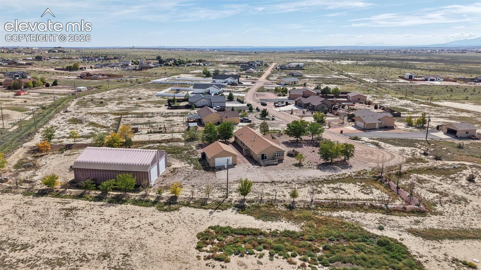Aerial perspective of a multi-structure property featuring a detached metal-sided workshop, a detached garage, and a residence with a shingled roof, set on a sprawling parcel