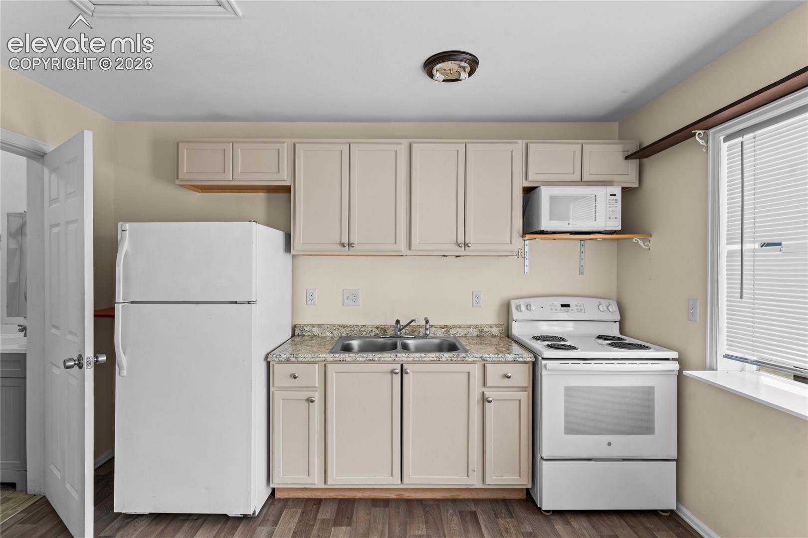 Compact kitchen featuring wood-finish flooring, light-colored cabinetry, a double basin sink, and a window with blinds