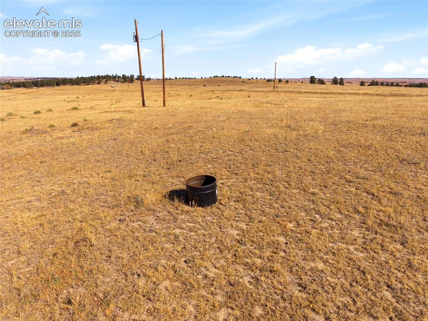 Expansive acreage featuring native grasslands, perimeter wire fencing, and utility poles
