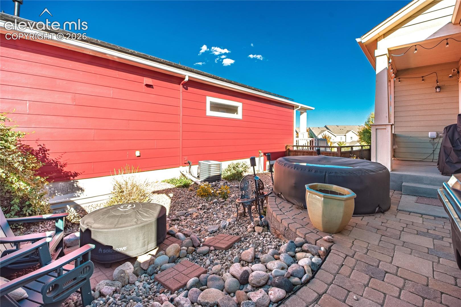 Exterior patio featuring decorative stone paver flooring, a raised masonry retaining wall, and low-maintenance rock landscaping