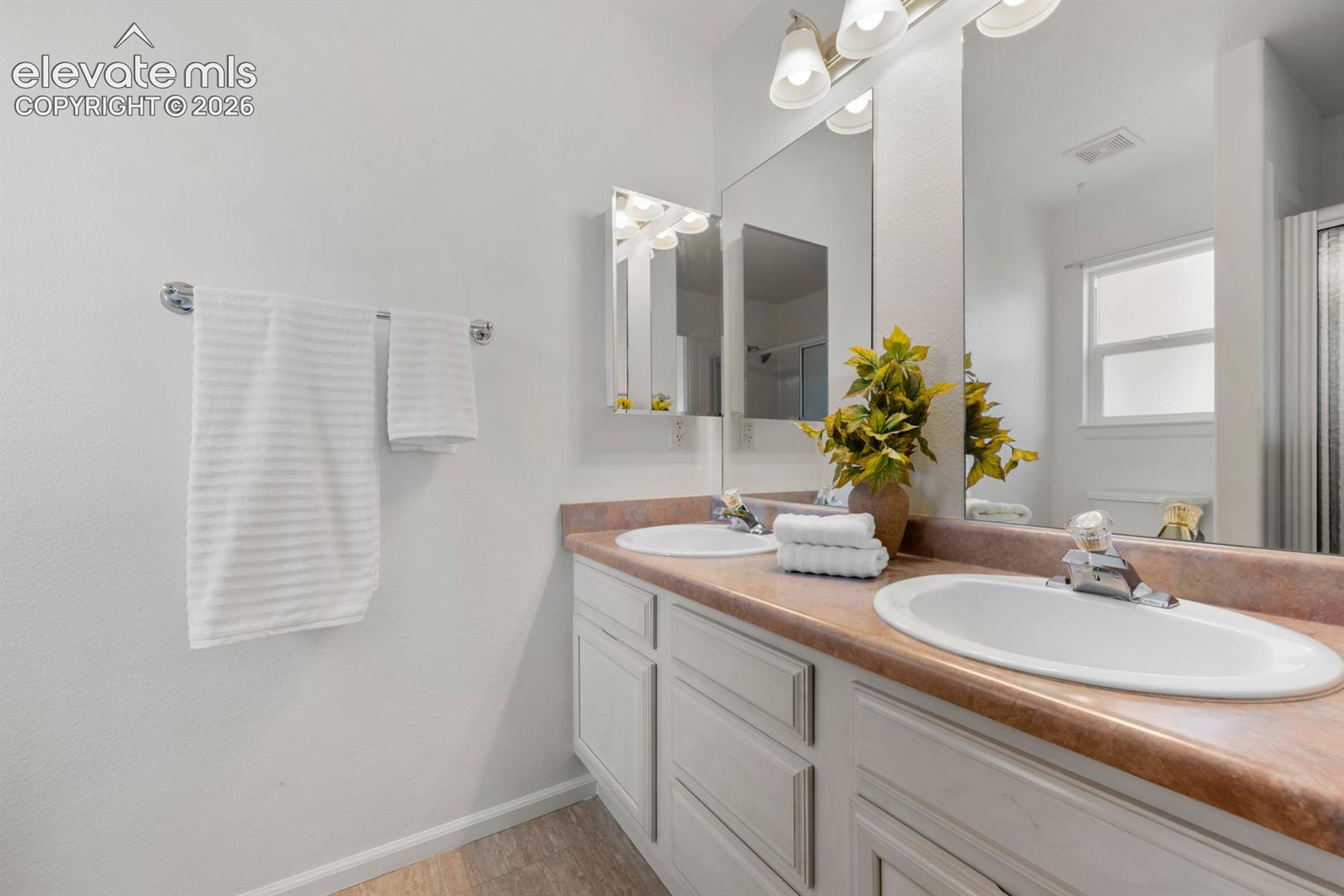 Dual-sink vanity with a solid-surface countertop, white cabinetry, integrated medicine cabinet, and wall-mounted multi-light fixture