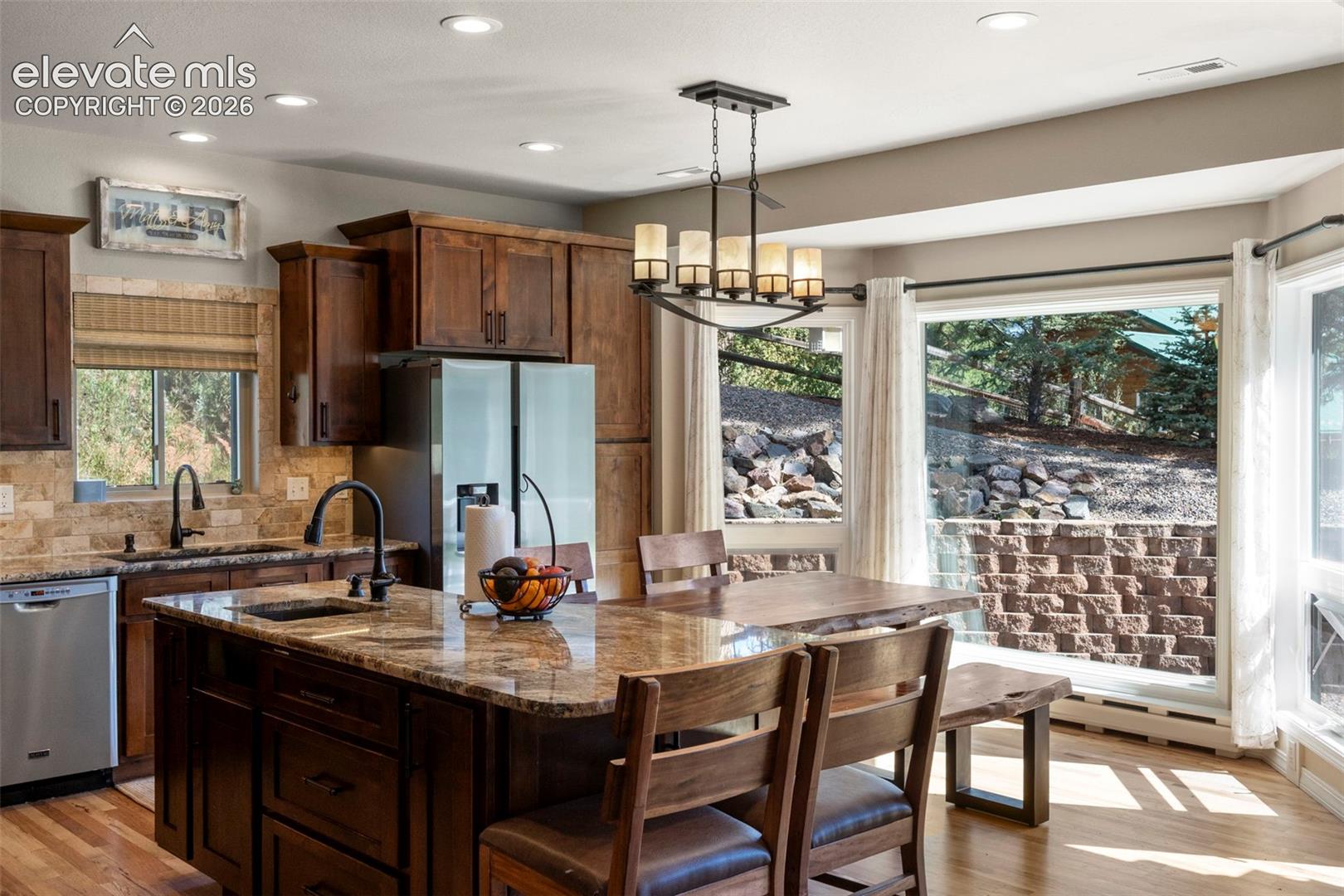 Kitchen featuring dark stone counters, light wood-style flooring, pendant lighting, appliances with stainless steel finishes, and a kitchen bar