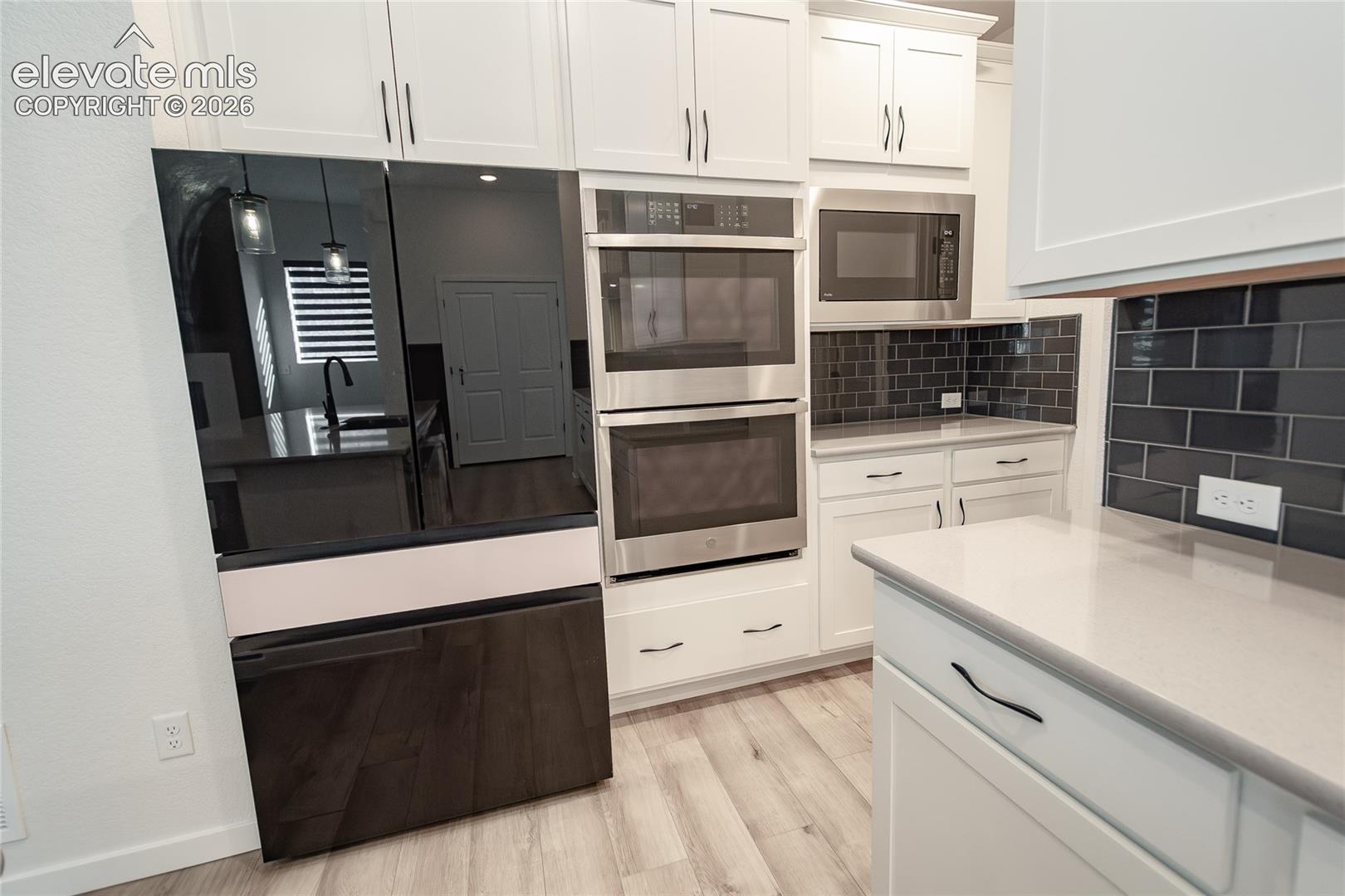 Kitchen featuring white shaker-style cabinetry, quartz countertops, a dark subway tile backsplash, stainless steel double wall ovens, and a dark-finish refrigerator