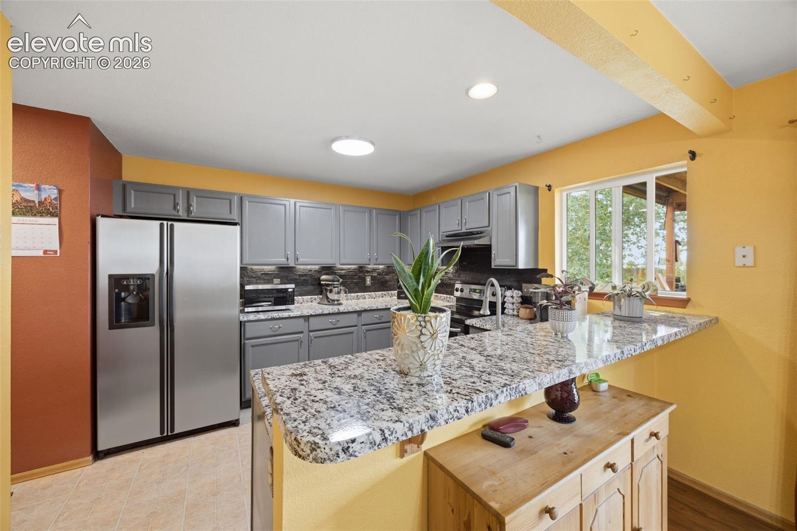 Kitchen featuring a stainless steel side-by-side refrigerator, grey cabinetry, granite countertops, and a tile backsplash