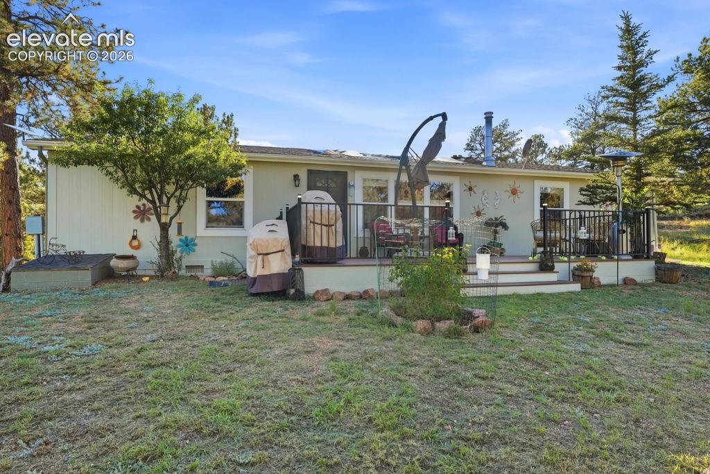 Rear exterior featuring a single-level deck with black railing, mature landscaping, and a natural grass area
