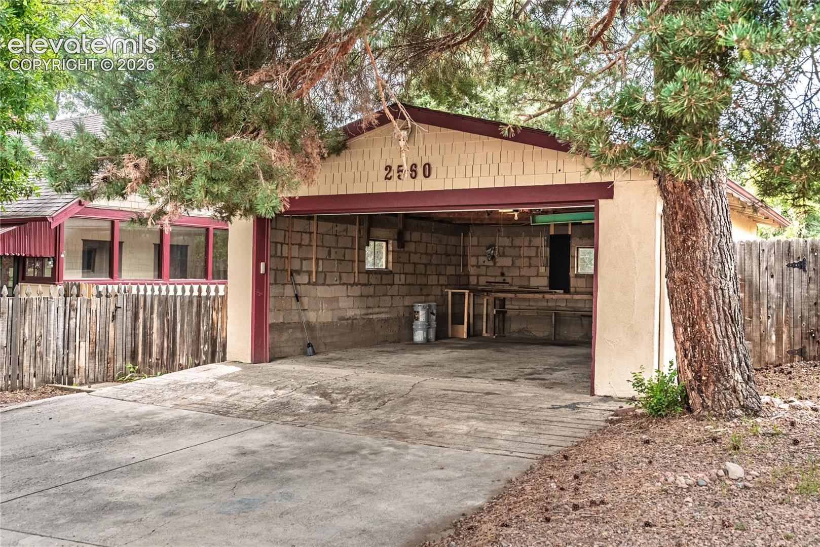 Detached garage with a wide concrete driveway, concrete block interior walls, and a wood picket fence
