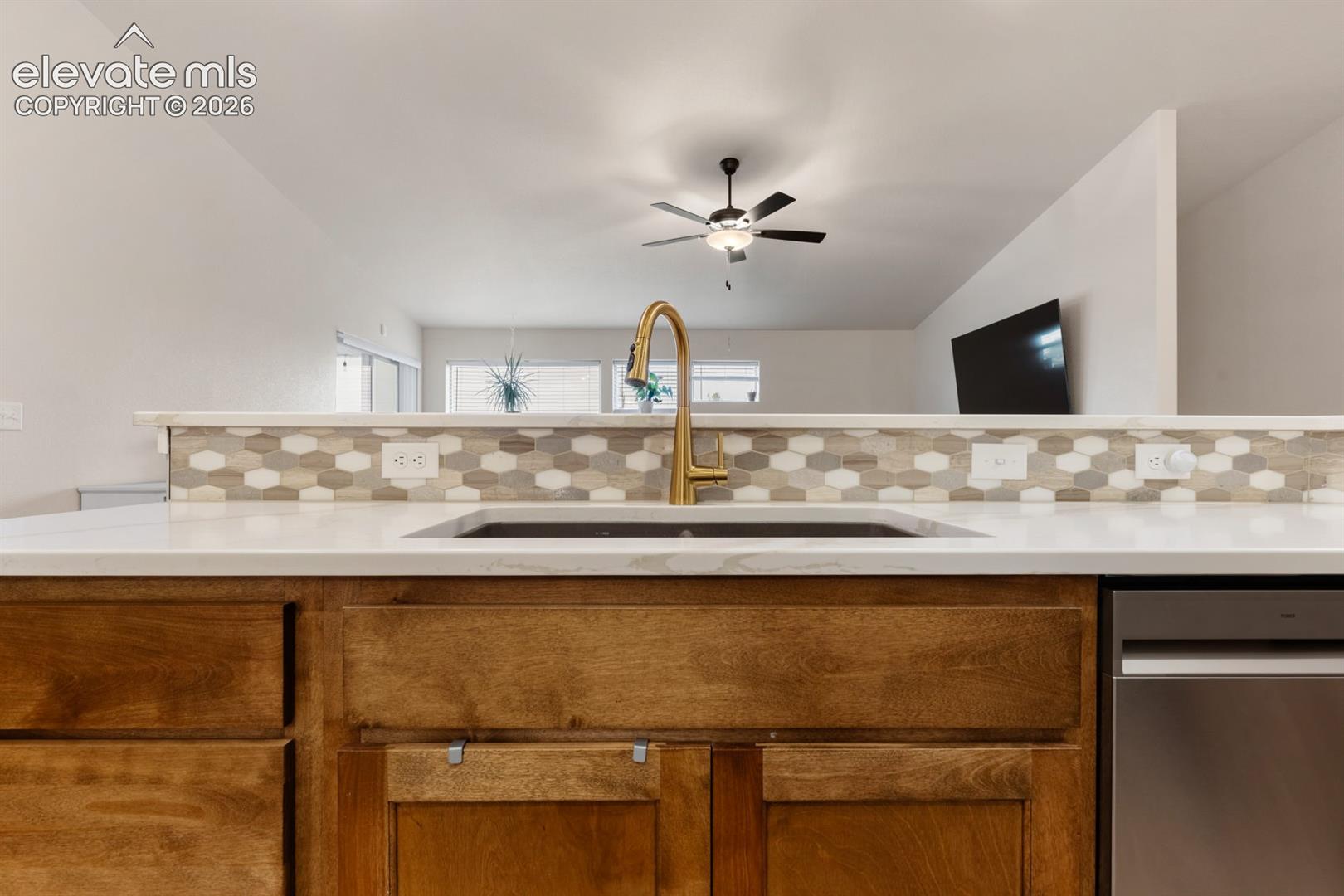 Kitchen island featuring a solid-surface countertop, an undermount sink with a brass-finish gooseneck faucet, hexagonal tile backsplash, and wood-finish cabinetry