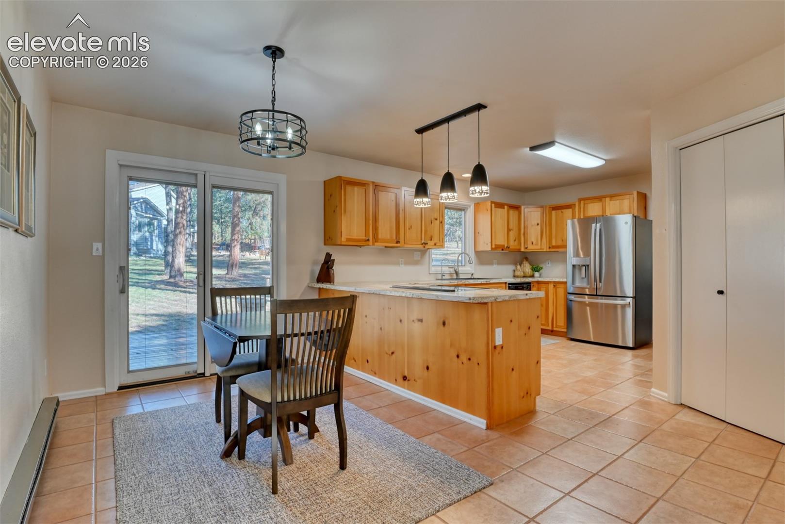 Kitchen featuring wood cabinetry, stone countertops, stainless steel refrigerator, tile flooring, and a sliding glass door