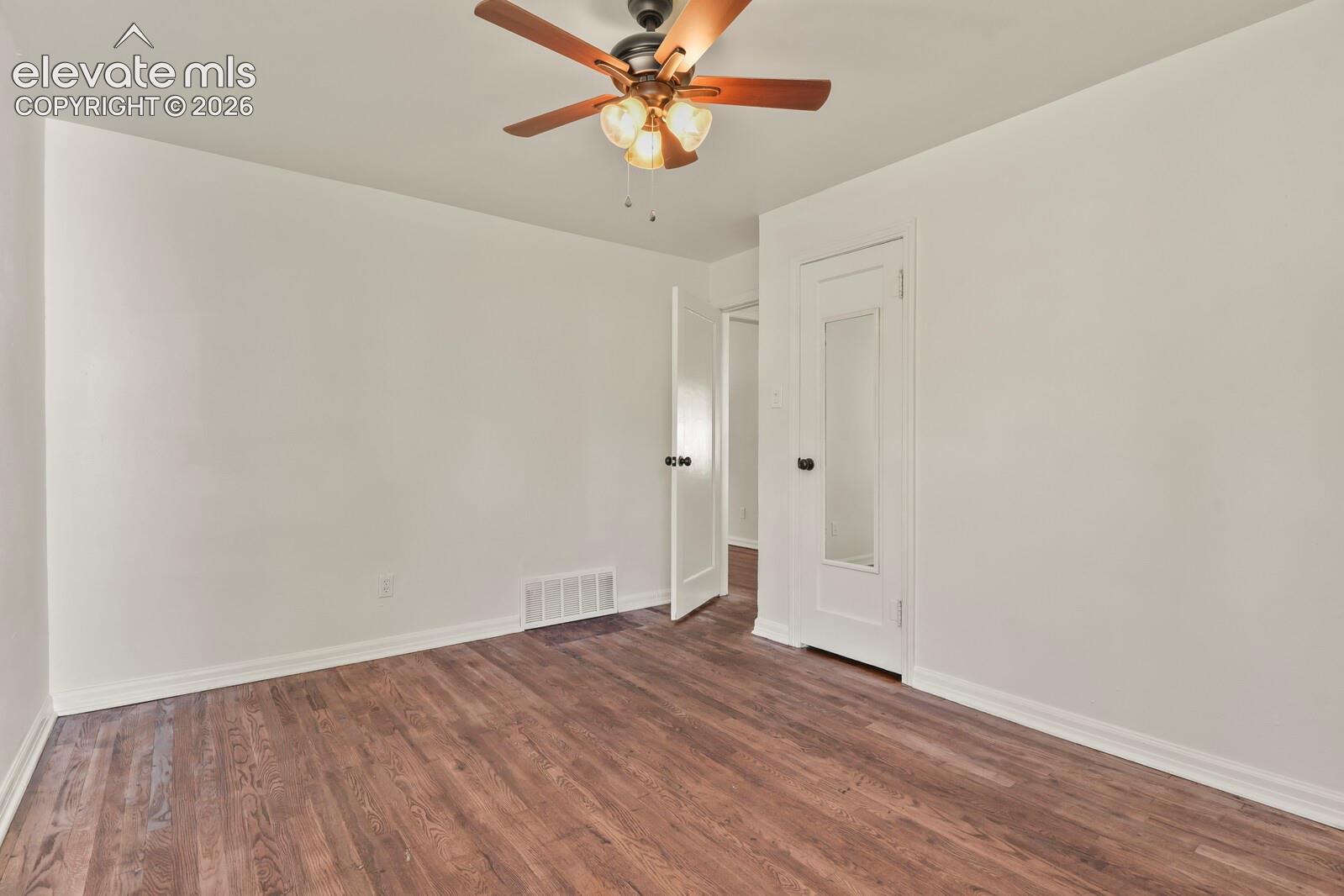 Room featuring wood-finish flooring, a ceiling fan with integrated lighting, and a solid-core door with a built-in vertical mirror panel