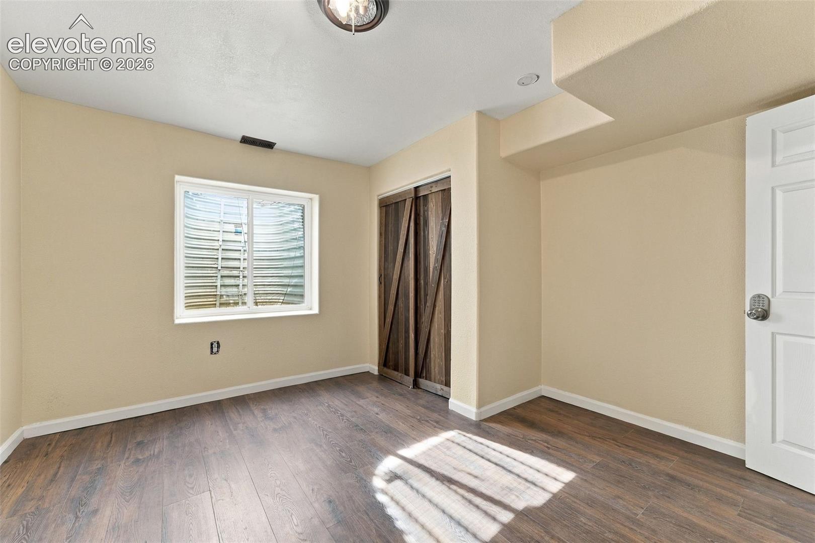 Room featuring wood-finish flooring, sliding barn-style closet doors, and an egress window with a metal window well