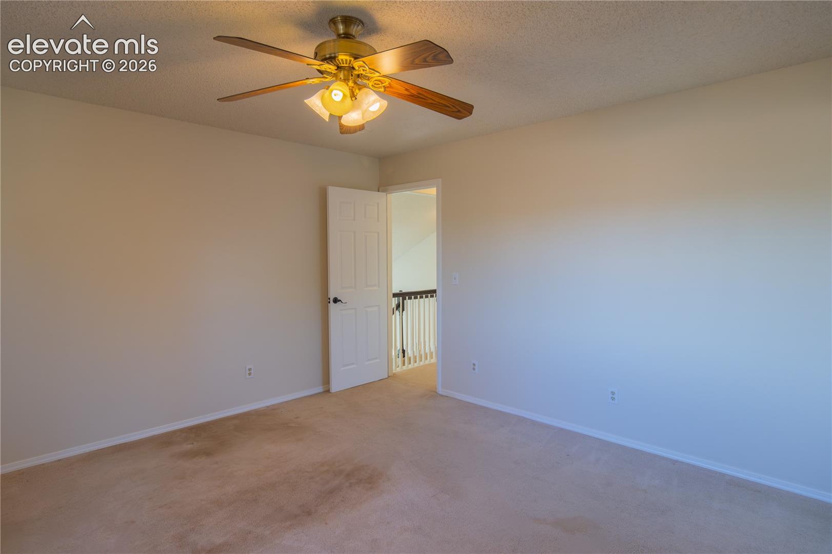 Comfortable upper-level primary bedroom with neutral carpeting and a lighted ceiling fan.