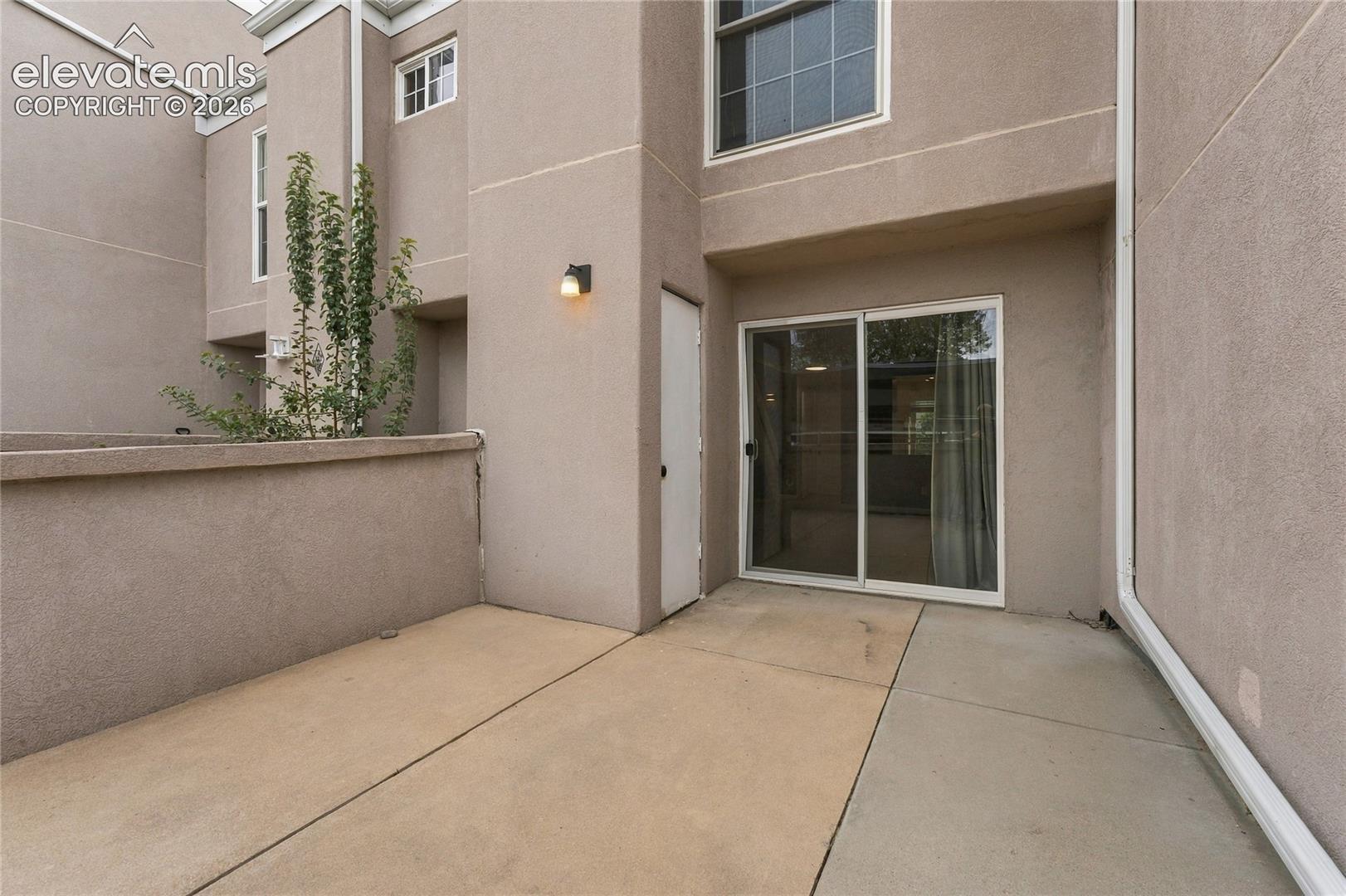 Private patio featuring a concrete floor, stucco perimeter wall, sliding glass door, and exterior wall-mounted light fixture