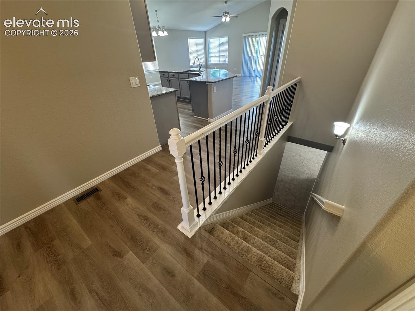 Staircase featuring a white handrail and wrought iron balusters, wood-finish flooring, vaulted ceilings, and kitchen cabinetry with a peninsula island