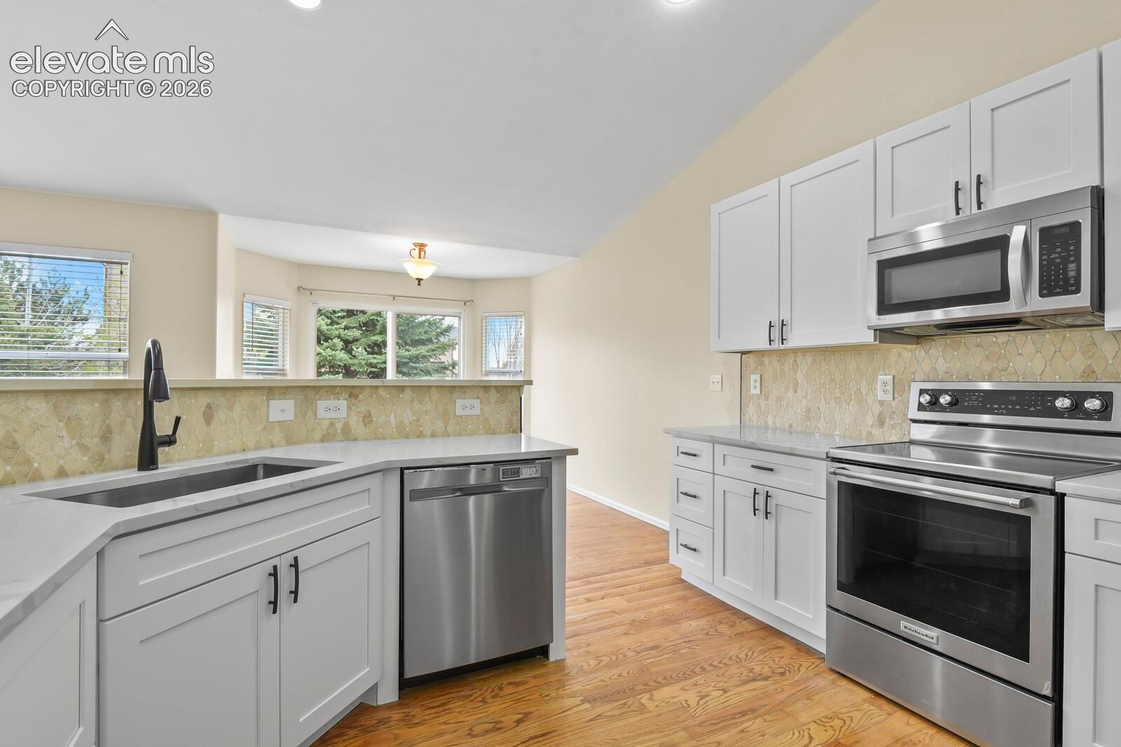 Contemporary kitchen featuring white cabinetry, light-toned countertops, and a full suite of stainless steel appliances including a built-in microwave, range, and dishwasher