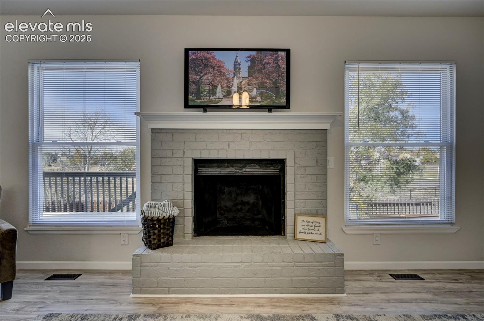 Painted brick fireplace featuring a classic white mantel and dual flanking windows with horizontal blinds