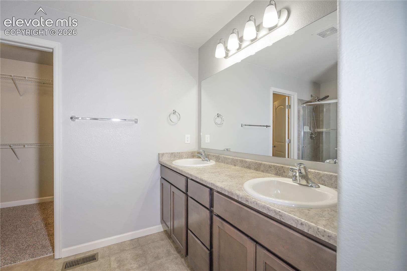 Dual-sink vanity with neutral countertop, full-width mirror, multi-light fixture, and walk-in closet with built-in shelving
