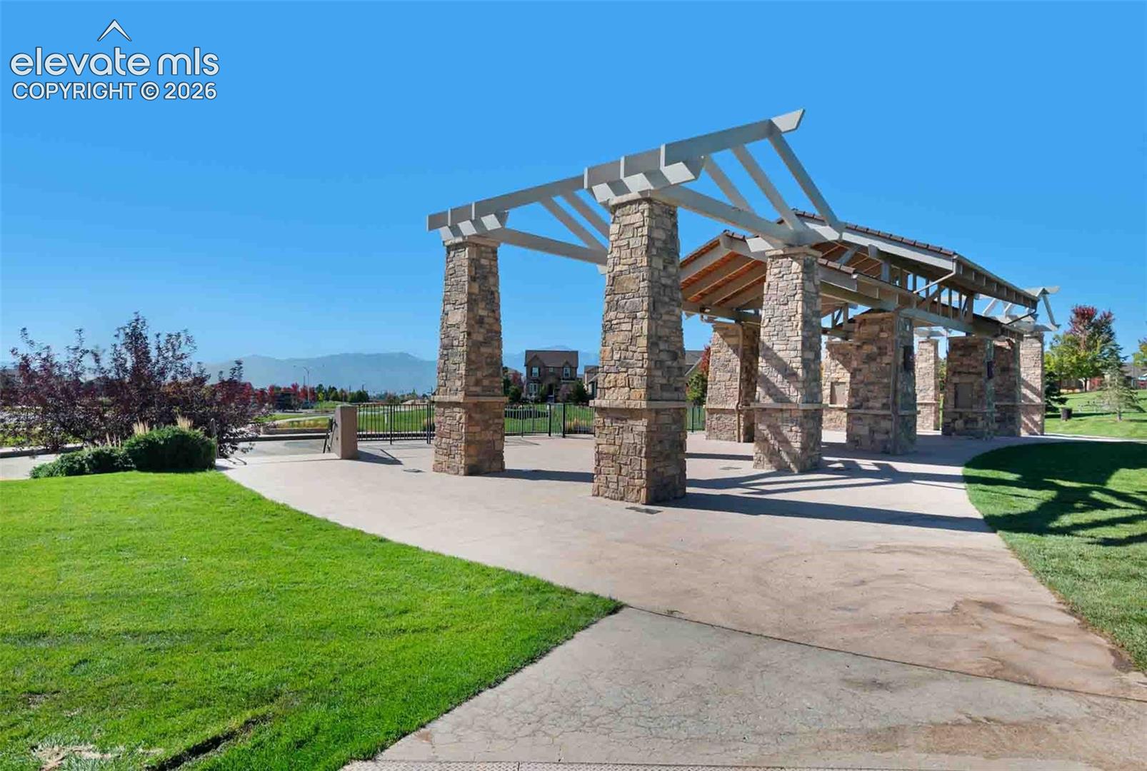 Outdoor pavilion featuring a pergola top, stone-clad pillars, concrete flooring, and manicured landscaping