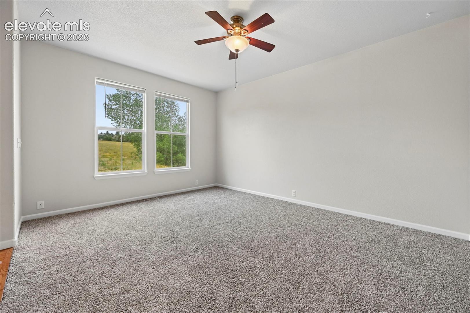 Spacious room featuring neutral paint, gray carpeting, a ceiling fan with integrated lighting, and two large windows