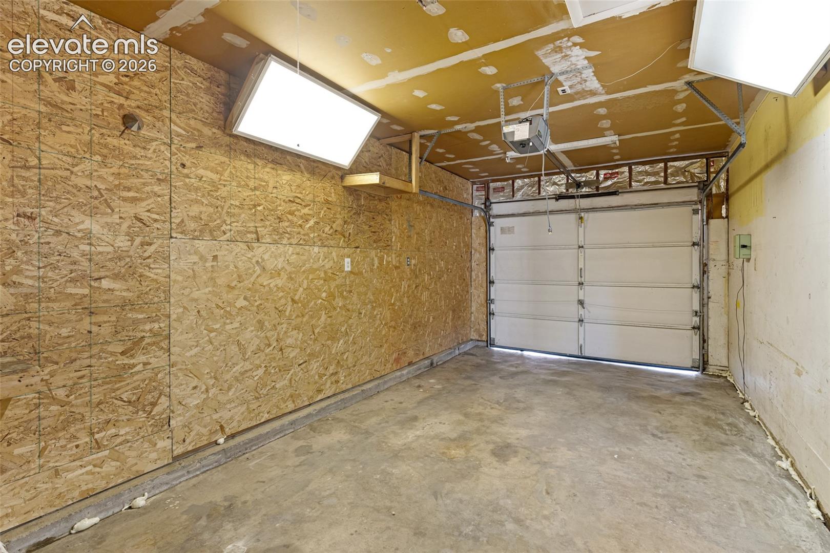 Spacious garage featuring concrete flooring, OSB-sheathed walls, overhead lighting with skylight panels, and an automatic garage door with steel frame construction